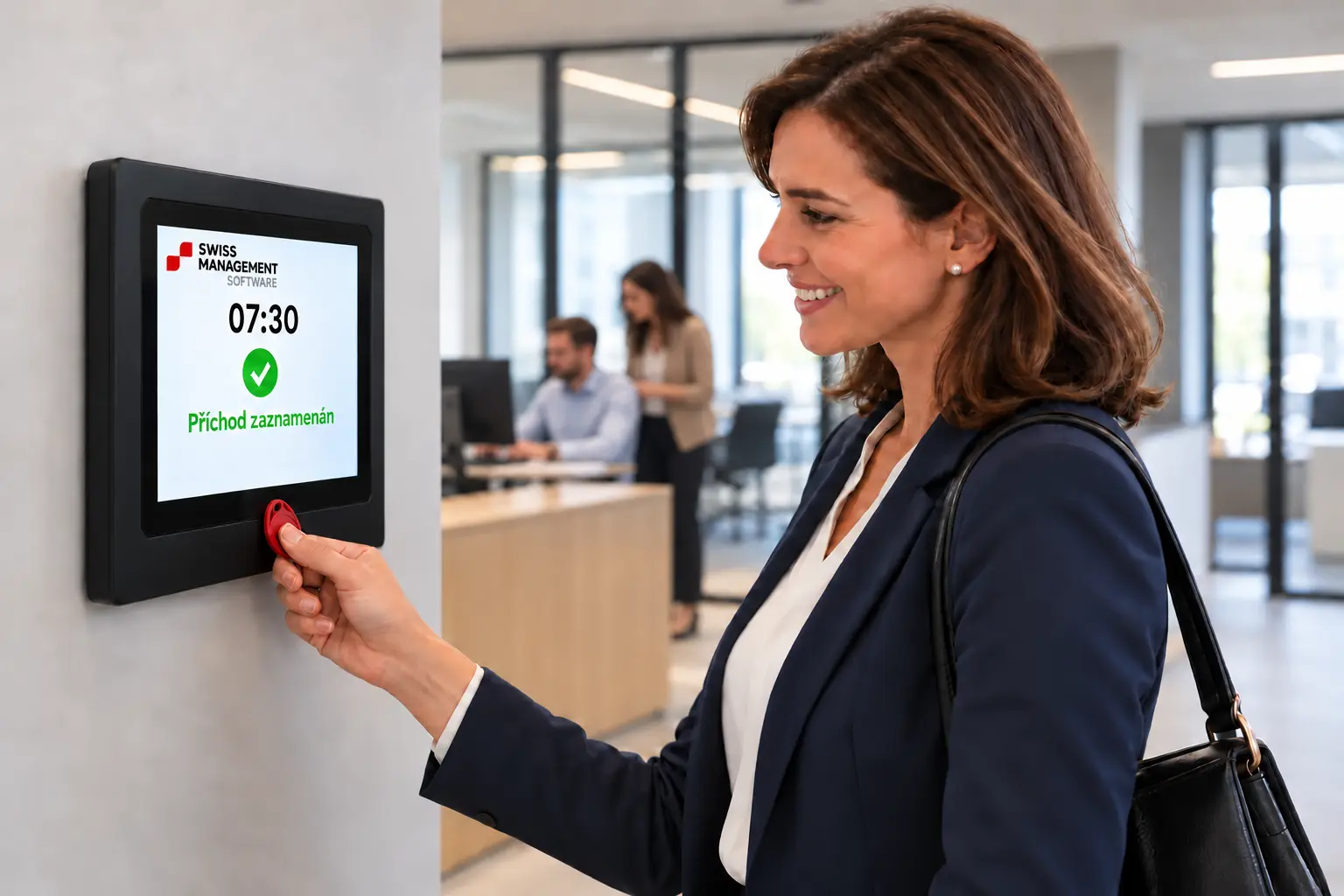 Elegantně oblečená zaměstnankyně má čip přiložený k terminálu Swiss Management Software, v pozadí pracují dva kolegové